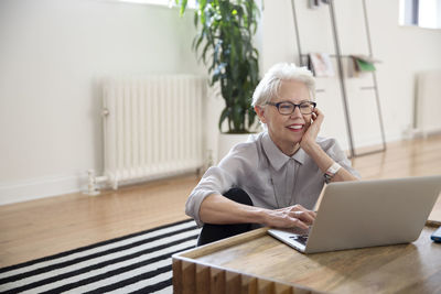 Senior businesswoman using laptop while sitting on carpet in office