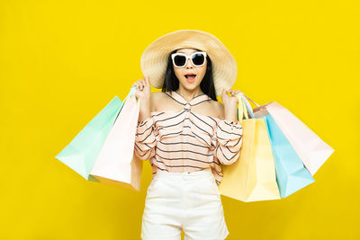 Mid adult woman wearing sunglasses against yellow background