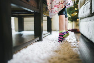 Low section of girl tiptoeing on rug by table at home