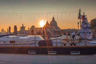 Sailboats moored in city against sky during sunset