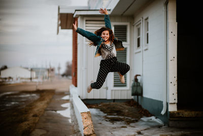 Portrait of girl with arms raised jumping against built structure