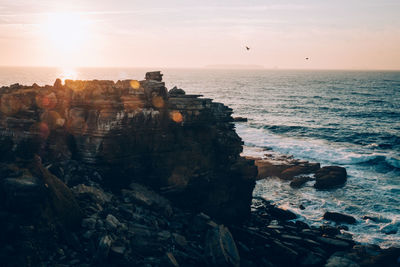 Scenic view of cliff by sea against sky during sunset