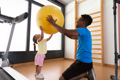 Black father and daughter exercising with fit ball