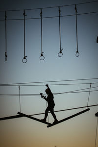 Low angle view of silhouette man hanging on cable against sky