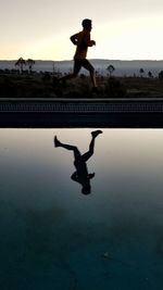 Reflection of silhouette man jumping in water at sunset