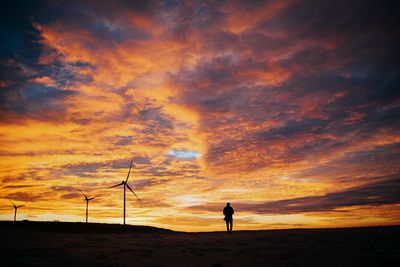 Silhouette man standing on land against cloudy sky during sunset