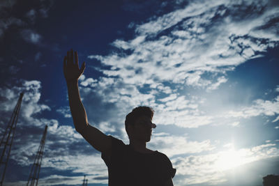 Low angle view of silhouette man standing against sky with a hand in the air