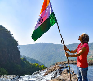 Woman standing on rock by mountain against sky with indian flag