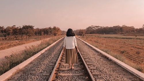 Rear view of woman walking on railroad track against clear sky