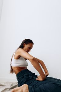 Side view of young woman sitting against white background