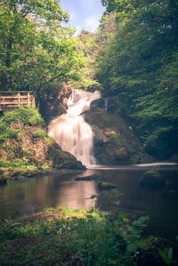 Scenic view of waterfall by river against sky