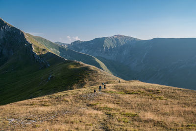 Hikers walking on mountains against clear blue sky