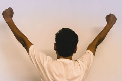 Rear view of man with arms raised standing against white background