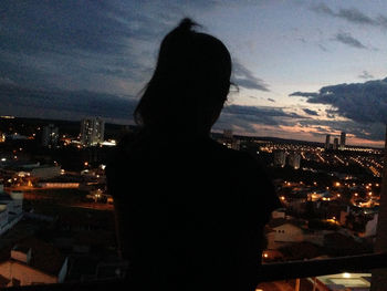 Rear view of silhouette woman looking at illuminated city buildings