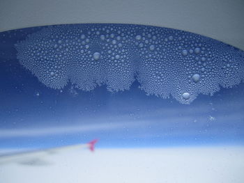 Close-up of wet glass window against sky