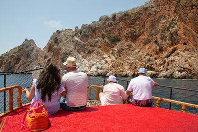 Rear view of people sitting on rock by mountain against sky