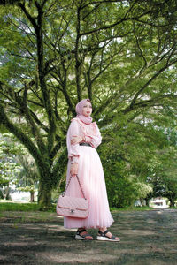 Woman with pink umbrella against trees in park