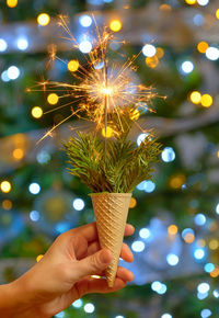 Cropped hand of woman burning sparkler with ice cream cone