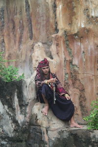 Young man in traditional clothing sitting on rock formation