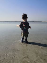 Boy standing at beach against sky