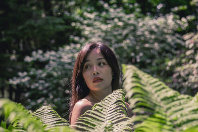 Young woman looking away while standing by plant