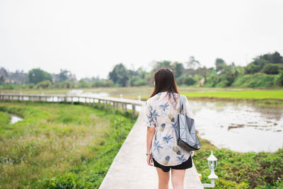 Rear view of woman walking on grass against clear sky