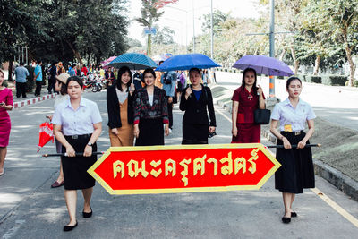Full length portrait of friends standing on tree in city