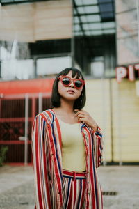 Young woman wearing sunglasses standing against built structure