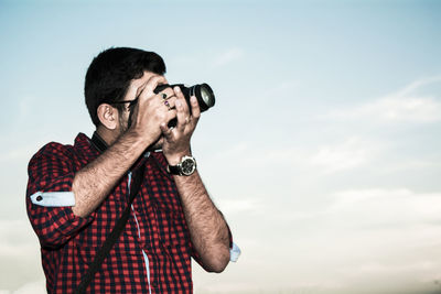 Young man photographing against sky