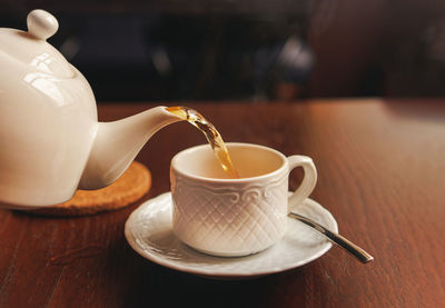 White cup with teapot. the hand holding the teapot pours tea into a pot standing on saucer 