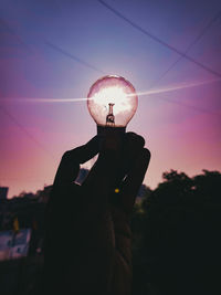 Silhouette person holding illuminated light against sky during sunset