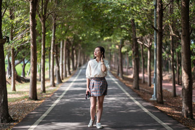 Full length of young woman walking on road along trees