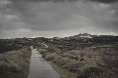 Dirt road leading towards mountains against sky