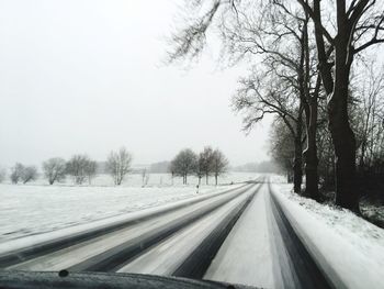 Snow covered road amidst trees against clear sky