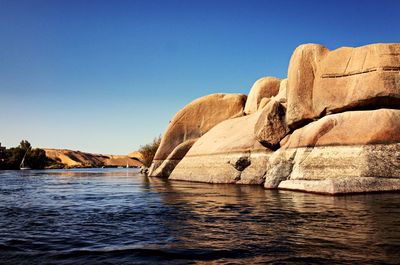 Rock formations in sea against clear blue sky