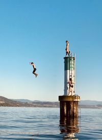 Men jumping in sea against clear blue sky