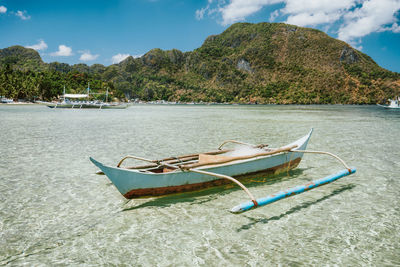 Boat moored on shore by sea against sky