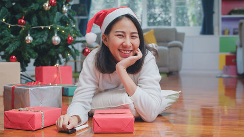 Smiling young woman sitting by christmas tree on floor