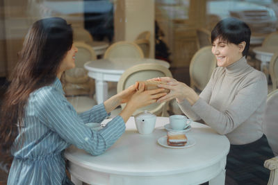 Cheerful women holding gift while sitting at cafe