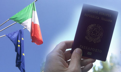 Midsection of person holding flag against blue sky