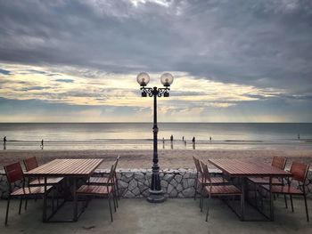 Chairs and table at beach against sky during sunset