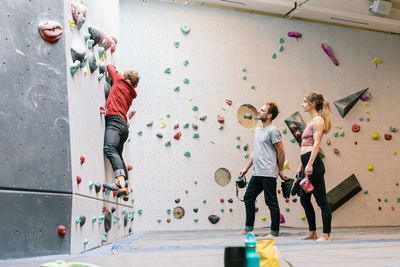 Side view of mature coach training male and female students for wall climbing in gym