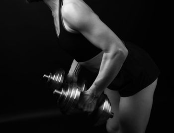 Midsection of woman holding dumbbells standing against black background