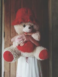 Woman holding teddy bear while standing against closed door