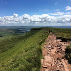 Rear view of friends hiking on hills against cloudy sky