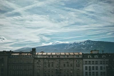 Buildings and mountains against cloudy sky