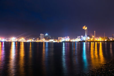 Illuminated buildings by sea against sky at night