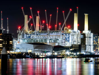 Illuminated city by river against sky at night