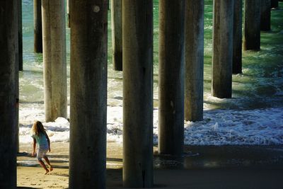 Rear view of girl walking under pier at beach