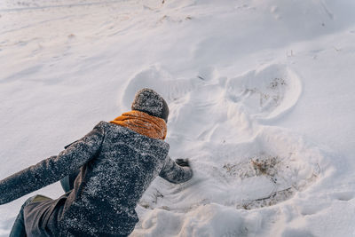 A woman in a snow-covered coat and hat draws a snow angel in the snow